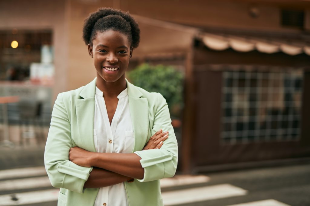 young african american businesswoman with crossed arms smiling happy at the city